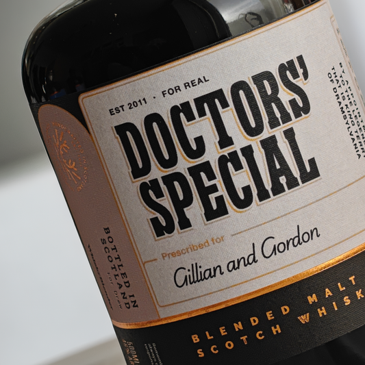 Close-up of a bottle label reading 'Doctors' Special' with 'Prescribed for Gillian and Gordon' and 'Blended Malt Scotch Whisk' on a dark bottle.
