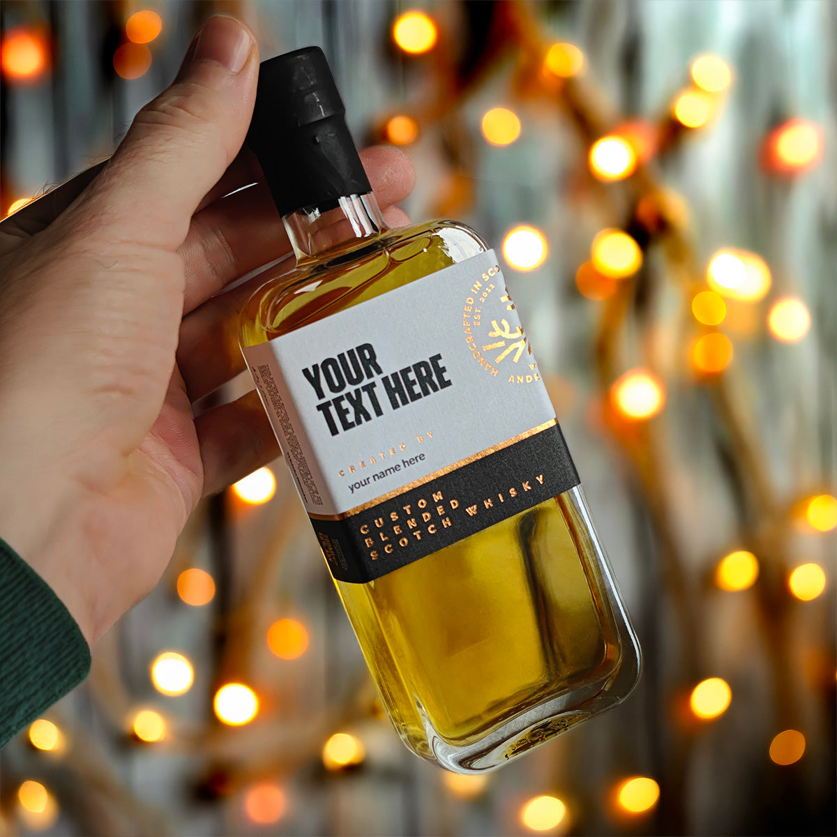 Hand holding a personalised 200ml whisky bottle in front of glowing fairy lights